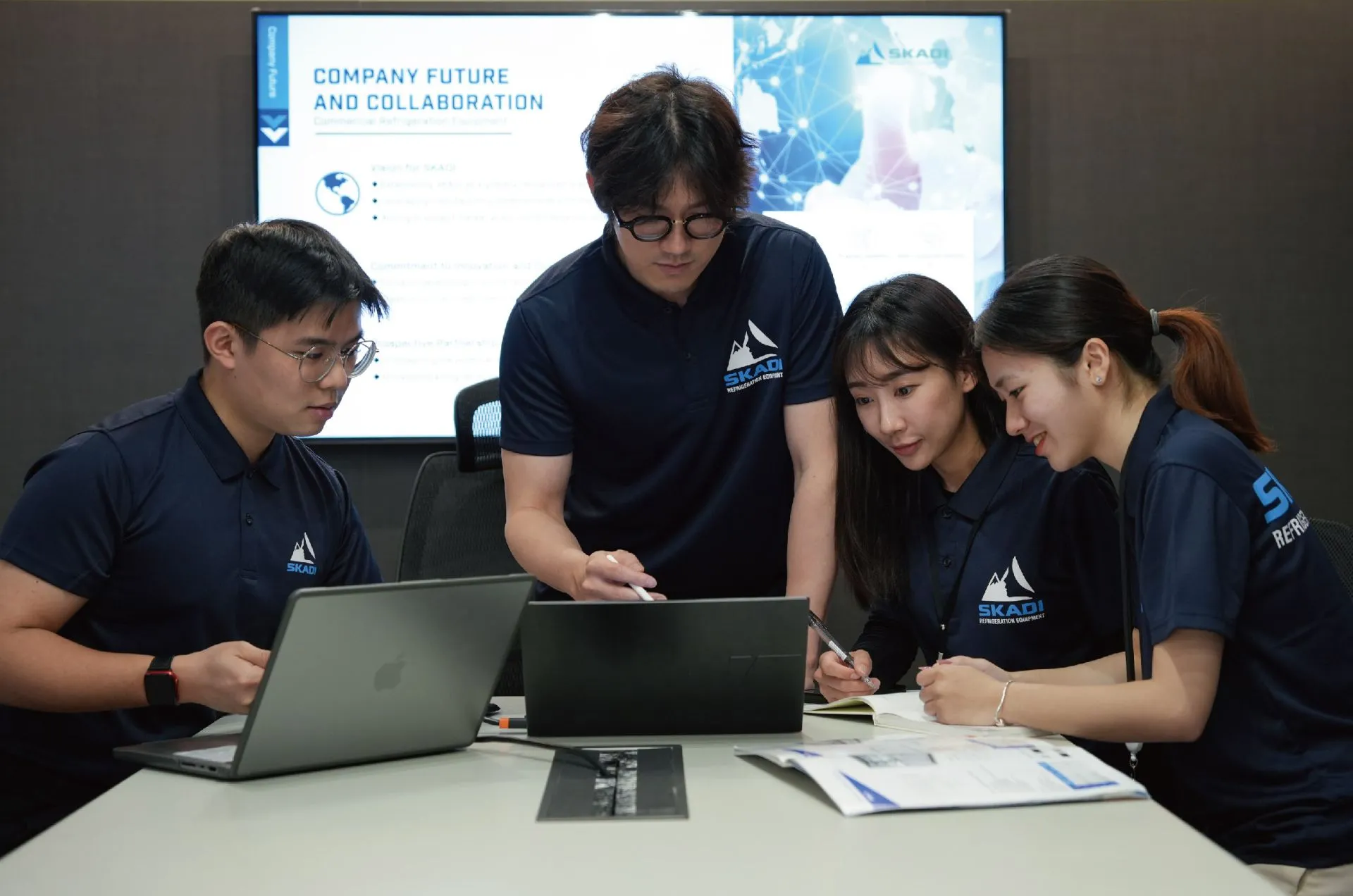 A team of four Skadi employees collaborating around a table with laptops and documents, discussing future company strategies and collaborations, representing the company's focus on teamwork and innovation.